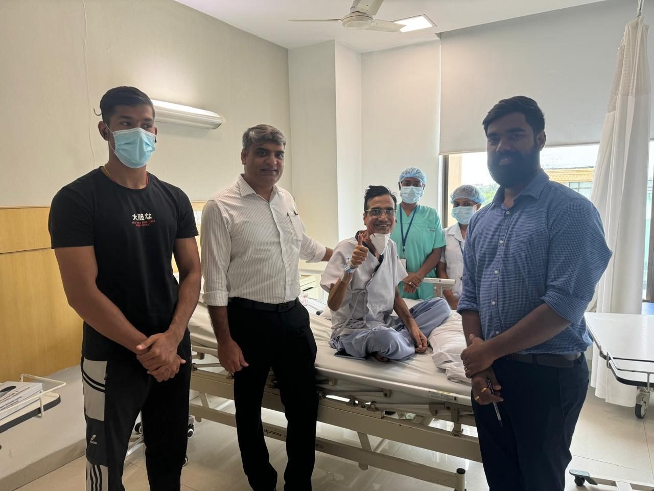 Patient giving a thumbs up from the bed with family, nurses and Dr Manoj Gupta